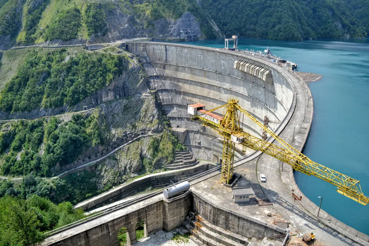 Aerial view of a tower crane working at a large concrete dam construction site beside a reservoir