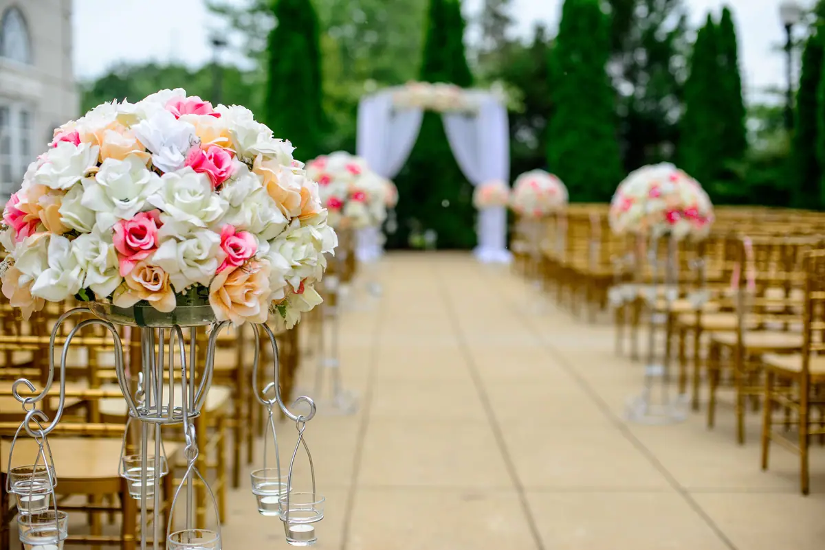 Outdoor wedding ceremony aisle lined with chairs and floral arrangements leading to an arch